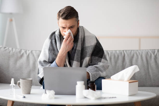 istock Man covered in blanket working online, sneezing nose 1313787521