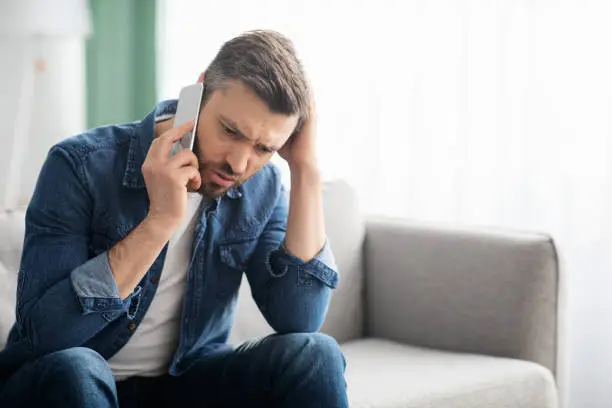 Photo of Worried middle-aged man having conversation on smartphone