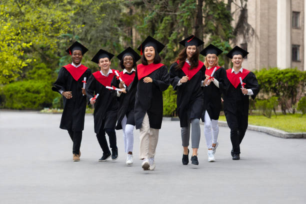 istock Cheerful multiracial students in graduation costumes walking by university campus 1313790163