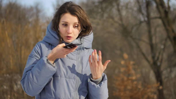 lady in blue coat sta inviando un messaggio vocale audio che spiega qualcosa sullo smartphone all'aperto parlando con l'assistente mobile. ragazza che usa il riconoscimento vocale e la dettatura dello smartphone - head in hands audio foto e immagini stock