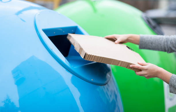 istock Waste Sorting. Female throwing cardboard box into blue recycle bin container outdoors 1313790585