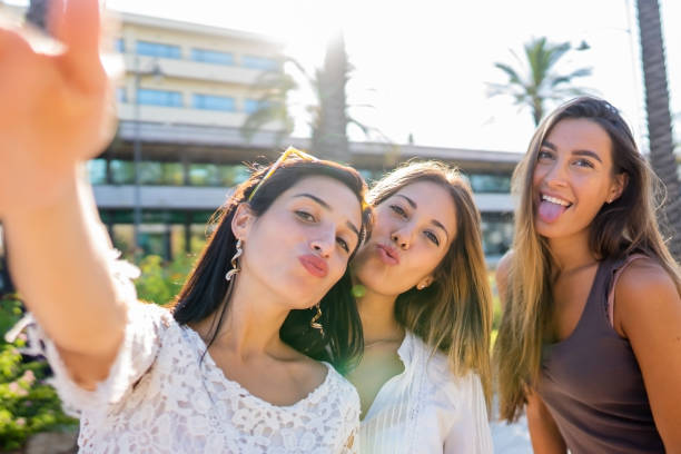 Three beautiful, funny playful girls have fun on vacation taking self portrait with smartphone making cheeky face . Carefree youth generation spending time on social network sharing picture and video tres chicas juguetonas hermosas y divertidas se divierten en vacaciones tomando autorretrato con teléfonos inteligentes haciendo cara descarada. generación juvenil despreocupada que pasa tiempo en la red social compartiendo imagen y video