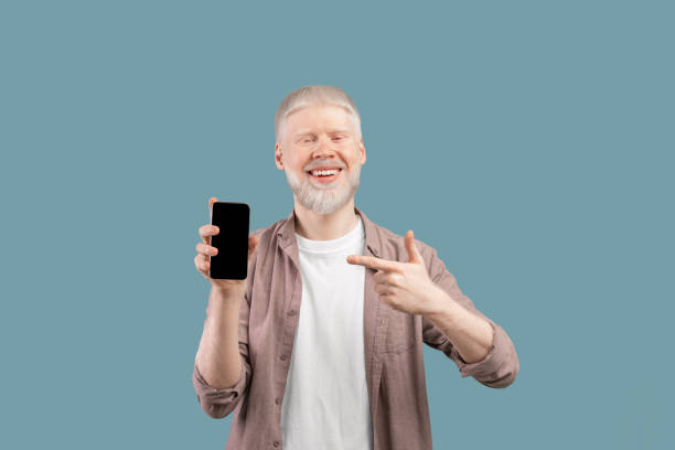 istock Check this app. Joyful albino guy holding and pointing finger at smartphone with black screen, studio background 1313791980