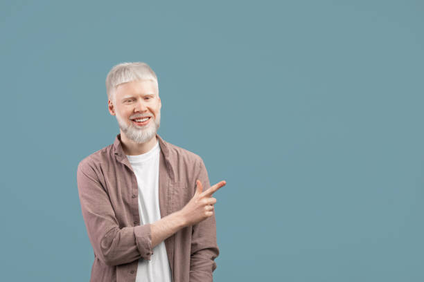 istock Cool offer. Confident albino man pointing at free space on turquoise studio background and smiling to camera 1313791993