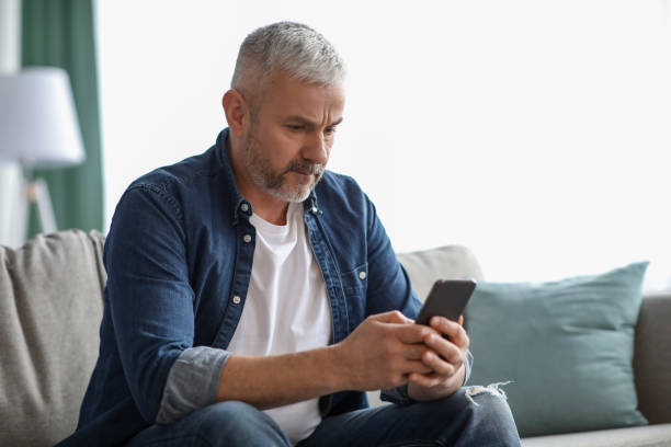 istock Grey-haired matured man sitting on couch, using mobile phone 1313792142