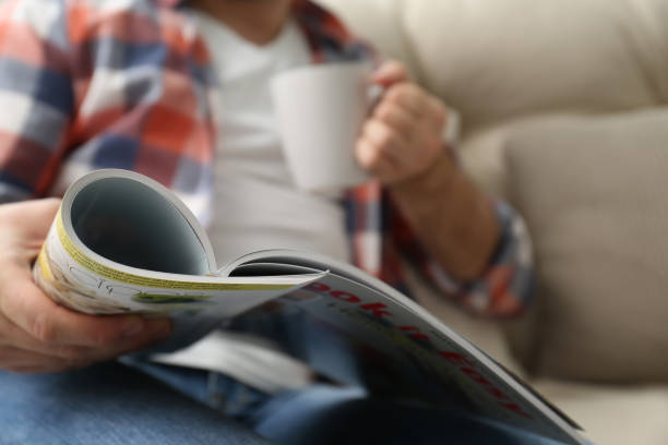 istock Man with cup of drink reading magazine on sofa, closeup 1313792384