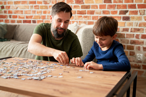 Boy solving jigsaw puzzle with father in living room at home