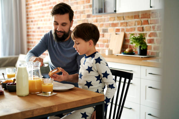 père et fils heureux ayant le petit déjeuner ensemble au matin - butter bread breakfast table photos et images de collection