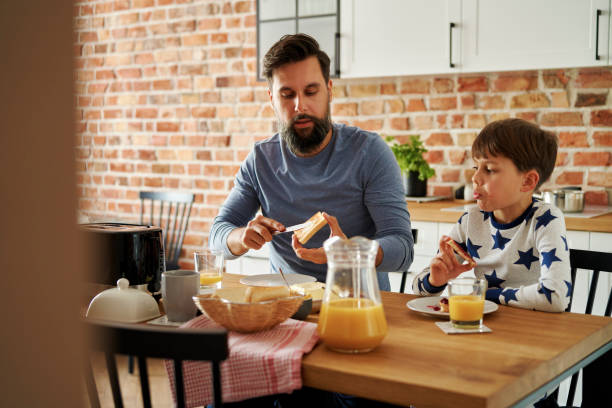 père et fils mangeant le petit déjeuner ensemble au matin - butter bread breakfast table photos et images de collection