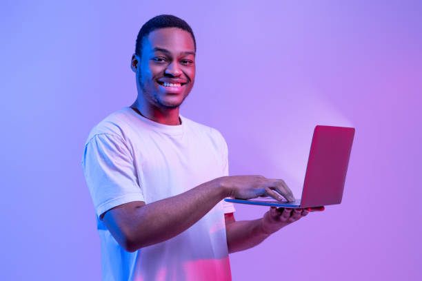 istock Online Work. Portrait Of Smiling African Guy Using Laptop With Glowing Screen 1313792930