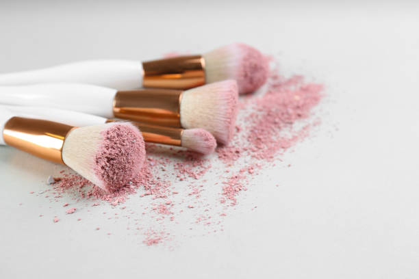 istock Different makeup brushes with crushed cosmetic product on light background, closeup. Space for text 1313793594