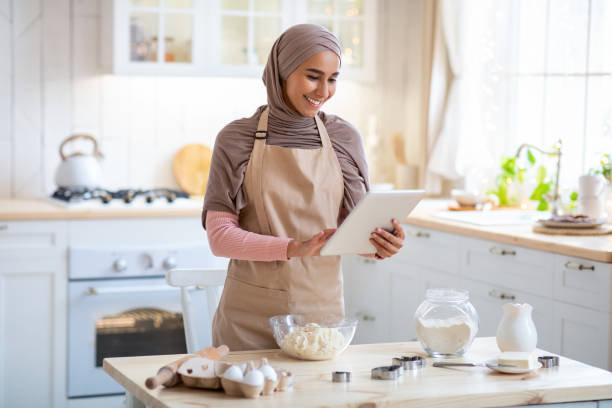 istock Happy Muslim Housewife In Hijab Using Digital Tablet In Kitchen While Baking 1313793932