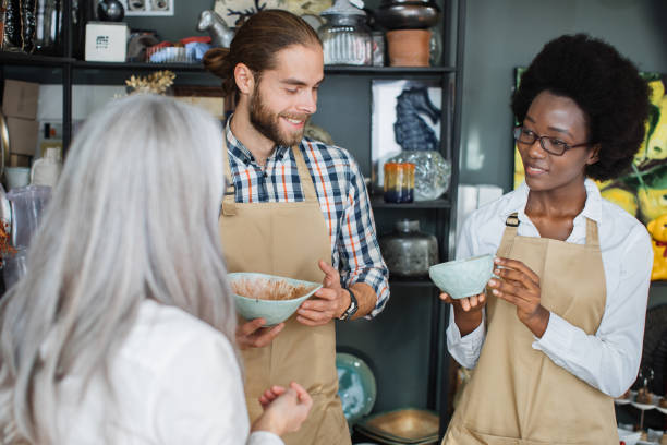 istock Two shop workers showing goods to female client 1313798113