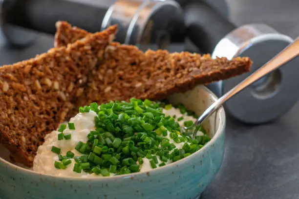 Post or pre workout meal with low fat cottage cheese, chives and wholegrain bread served in a bowl with dumbbells in the background