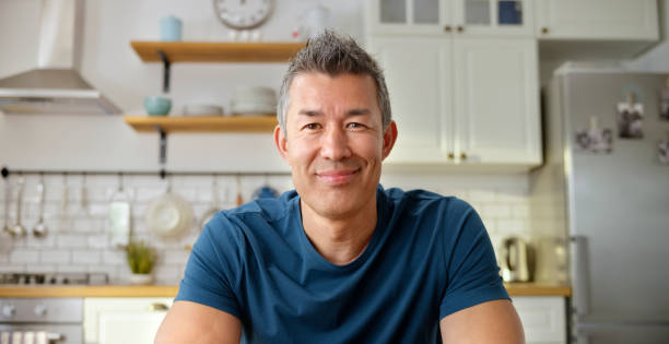 Mature man having a video call in kitchen Portrait of smiling mature man talking on a video call in kitchen during COVID-19 pandemic. 45 49 years stock pictures, royalty-free photos & images