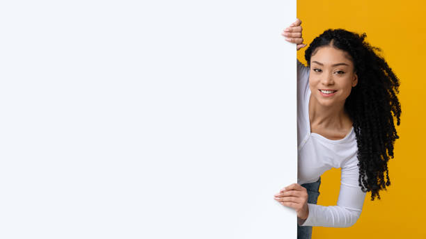 istock Positive Black Lady Peeking Out Of Blank White Advertisement Board 1313802692