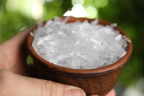 Woman holding bowl with menthol crystals against blurred background, closeup