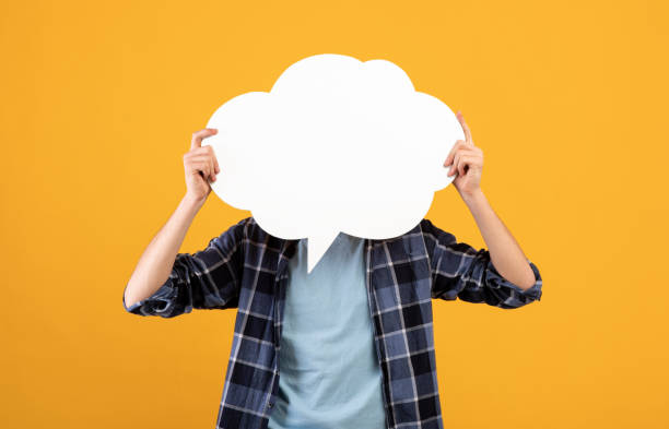 istock Unrecognizable young man holding blank speech bubble in front of his face over orange background, mockup for design 1313806200