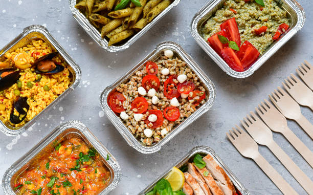Different aluminium lunch box with healthy natural food tray with pasta pesto, spelt, paella, quinoa, chicken salad, curry on gray table Food delivery . airlines food. Different aluminium lunch box with healthy natural food tray with pasta pesto, spelt, paella, quinoa, chicken salad, curry on gray table. Airline Meals and Snacks convenience food stock pictures, royalty-free photos & images