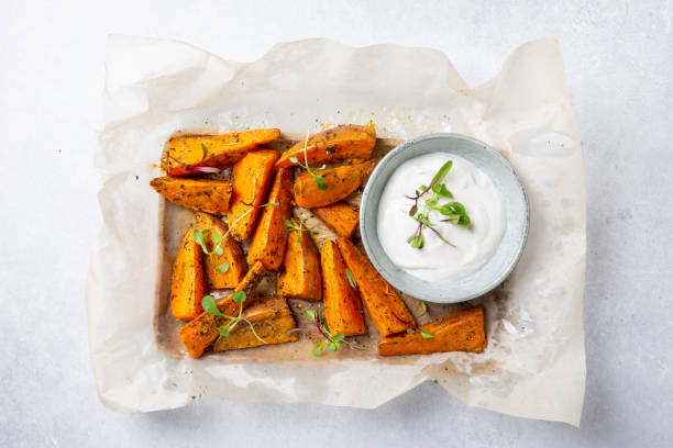 cuñas de batata. batata al horno al horno con hierbas servidas con salsa blanca sobre fondo gris. concepto de comida vegetariana saludable. vista superior. - sweet potato french fries yam baked fotografías e imágenes de stock