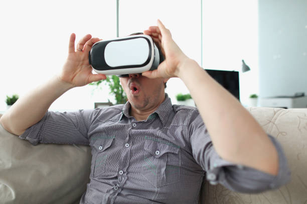 istock Surprised man wearing virtual reality glasses sitting on couch at home 1313815479