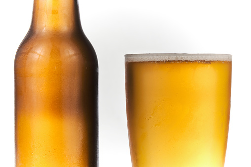 Brown beer bottle and a glass of beer in a white background. Beer brown bottle with drops and a full glass of beer isolated in white background