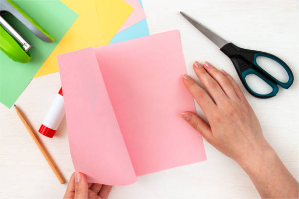 istock Empty pink paper with place for text. Colored paper, stapler, scissors, scissors, pencil on a white table. Children's craft card for mother's day. Step-by-step instruction. Step 11. 1313817640