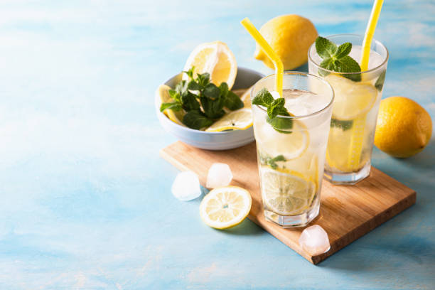 istock Two glass with lemonade or mojito cocktail with lemon and mint, cold refreshing drink or beverage with ice on blue background. Copy space 1313820235