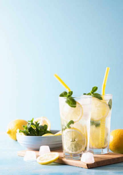 istock Two glass with lemonade or mojito cocktail with lemon and mint, cold refreshing drink or beverage with ice on blue background. Copy space 1313820245