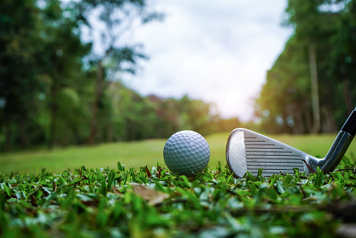 Golf ball on green grass ready to be struck on golf course background. Golf clubs and golf balls on a green lawn in a beautiful golf course with morning sunshine. Ready for golf in the first short.