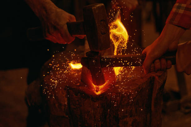 Blacksmiths hit molten metal with hammers close up Blacksmiths forging in smithy. Close up of hands of craftsmen hit molten metal detail with hammers into burning fire on wooden timber. Handmade metal work idea. Concept of handicraft blacksmith shop photos stock pictures, royalty-free photos & images