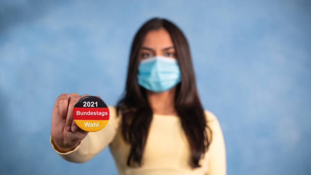 Young woman with a mask stretches out her arm and holds a election button in the German national colors, with the statement - 2021 Bundestagswahl. (2021 Federal election) Federal election Germany. chancellor of germany photos stock pictures, royalty-free photos & images
