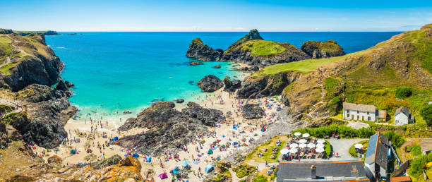Cornwall crowds of bathers on Kynance Cove beach panorama UK Crowds of tourists enjoying the summer sunshine amongst the sea stacks and rocky cliffs overlooking the turquoise ocean and idyllic sandy beaches of Kynance Cove, Cornwall, UK. marazion photos stock pictures, royalty-free photos & images