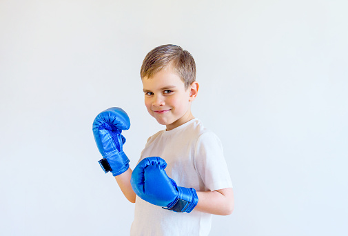 Smiling boy in boxing gloves stands in a fighting stance. Sports and self-defense