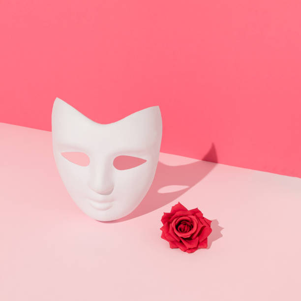 istock White costume ball face mask and red rose with sunlight shadow on bright pink background. Minimal abstract concept. 1313831634
