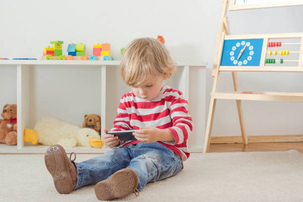 istock Cute little child using a smartphone while sitting on the floor at home. Digital device and screen time addiction, technology in the hands of children concept. 1313838502