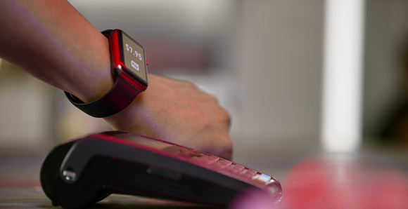 Close up of woman's hand making contactless payment with a smart watch.\nGraphics were created by the contributor.