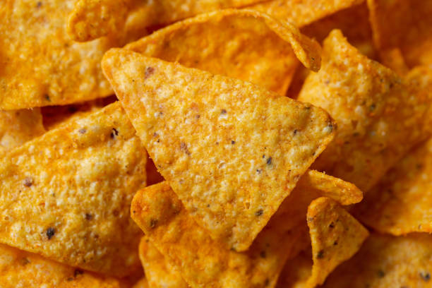 Crispy corn chips, triangular-shaped nachos with a cheese flavor. Fast food close-up Mexican Corn Chips triangle-shaped nachos with cheese flavor nacho chip photos stock pictures, royalty-free photos & images