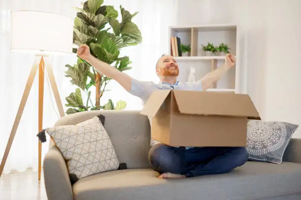 Photo of man sit on couch with joy opens carton box feel happy
