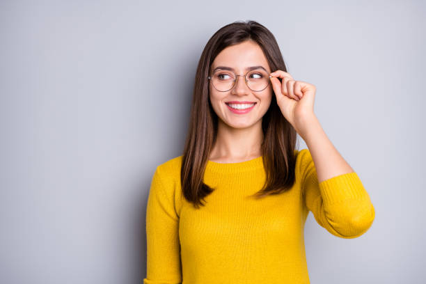 ritratto di attraente ragazza intelligente allegra che tocca le specifiche guardando da parte lo spazio di copia isolato su sfondo di colore grigio - aside foto e immagini stock