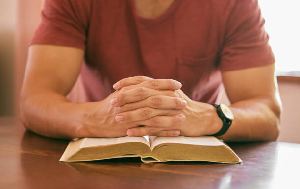 istock Shot of a young man with hands clasped above a bible at a table 1313851399