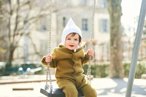 Outdoor portrait of cute toddler kid having fun on playground, wearing warm jumpsuit