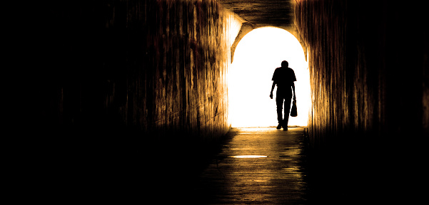 Old man walking through tunnel silhouetted representing end of despair long journey