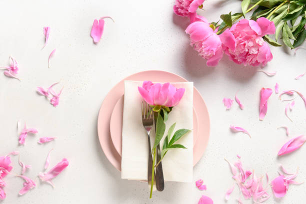 Romantic table setting with pink peony flowers on a white table. View from above.
