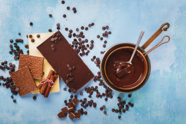 istock Melted chocolate in copper pan and  bars of dark and white chocolate beside on rustic blue surface. Top view, blank space 1313856499