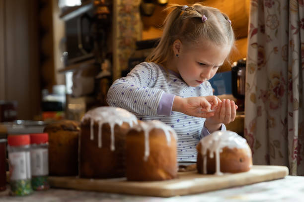 criança ajuda mãe decorar tradicional europa oriental bolo de páscoa russo e ucraniano kulich decorado com doce de açúcar cobertura em mesa de madeira raio de luz solar da manhã. saboroso pão de paska ortodoxo artesanal - bread food baked 7 grain bread - fotografias e filmes do acervo