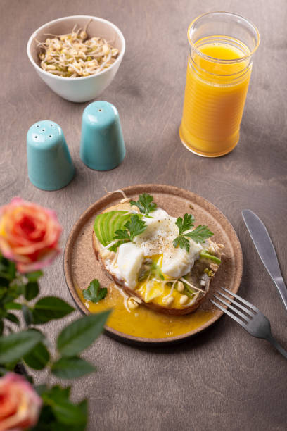 istock Light summer breakfast - sandwich with avocado, cottage cheese, sprouted beans and poached egg with orange juice on the table 1313865299