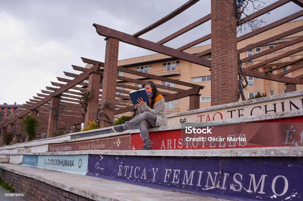 View from below of a woman reading a book, sitting on bleachers that look like books. One can read titles such as ethics and feminism, tao, Aristotle ... A view from below of a woman reading a book, sitting on bleachers that look like books. One can read titles such as ethics and feminism, tao, Aristotle ... Philosophy Stock Photo
