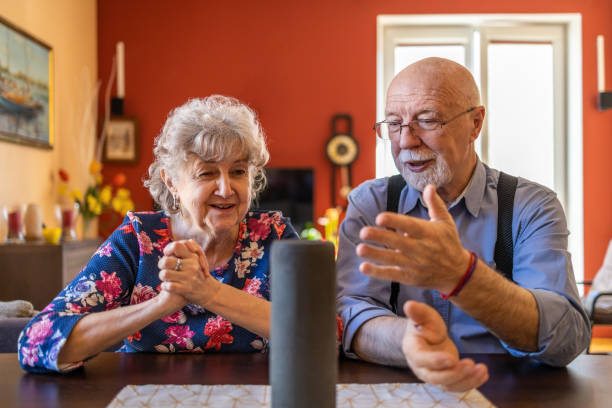 pareja de ancianos emocionados usando un asistente virtual en casa - senior couple audio fotografías e imágenes de stock