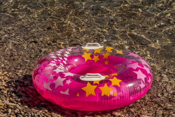 istock Summer beach composition. Pink  inflatable float with stars on pebble, shingle, boulder sea  background, trendy summer sea concept. Soft focus. 1313880448